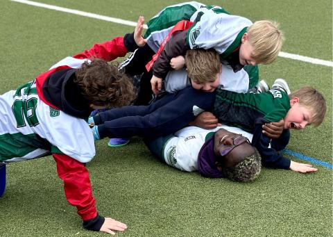 Das Bild zeigt ein paar Kinder, die sich stürmisch, zum Jubel, auf einen Werwachsenen schmeißen.